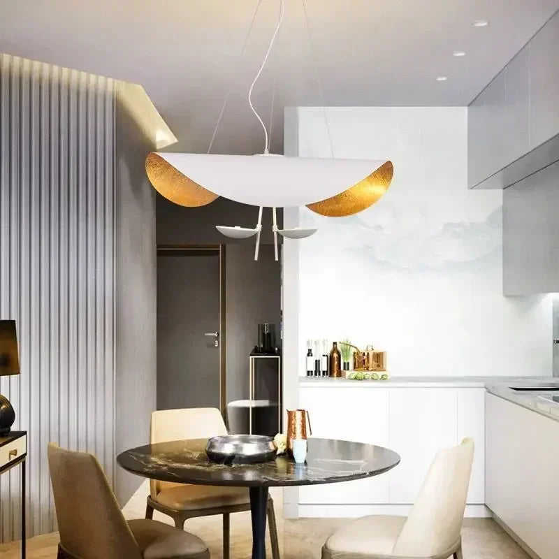 A bright kitchen area with a white and gold leaf wave pendant light hanging over a circular dining table.