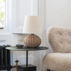 Woven rattan table lamp with a spherical base and fabric shade on a small round table in a living room setting.