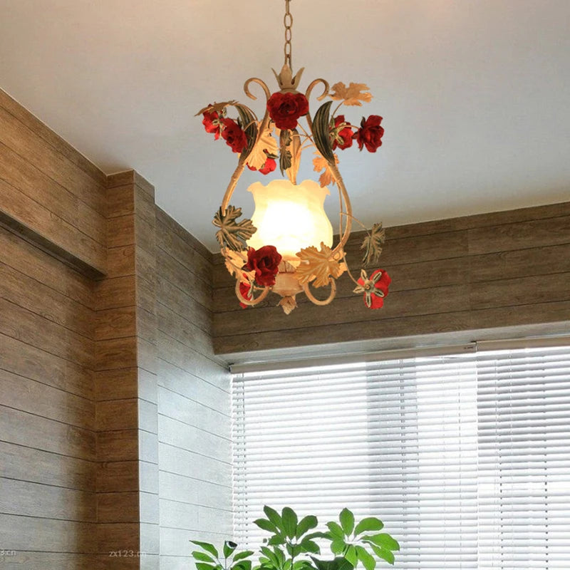 A gold floral pendant light with red rose accents hanging in a room with wood-paneled walls and blinds.