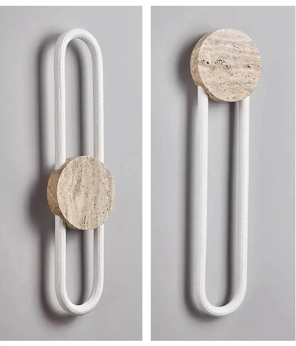 A wall sconce featuring a round stone piece and a U-shaped light element, shown against a grey wall.