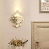 Matte white resin wall sconce with a floral design, casting upward light.