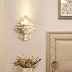 Matte white resin wall sconce with a floral design, casting upward light.
