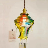 Single rainbow swirled glass droplet pendant light hanging against a white wall with photos attached.