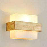 A modern wall sconce featuring a rectangular wooden bar horizontally mounted between two frosted glass rectangular diffusers, with warm light emanating from within.