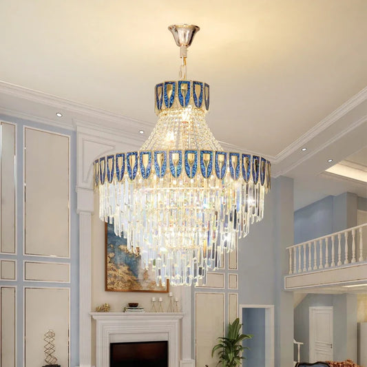 A large, ornate tiered chandelier with cascading crystals and a gold-toned frame, illuminated in a spacious, well-lit room.