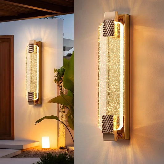 Gold wall sconce with textured bubble crystal diffuser mounted on a white wall, casting warm light.