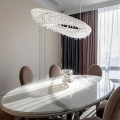 A large oval crystal chandelier hanging above an oval marble dining table.