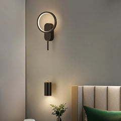 Modern wall sconce on a gray wall with a bed and plant in the foreground