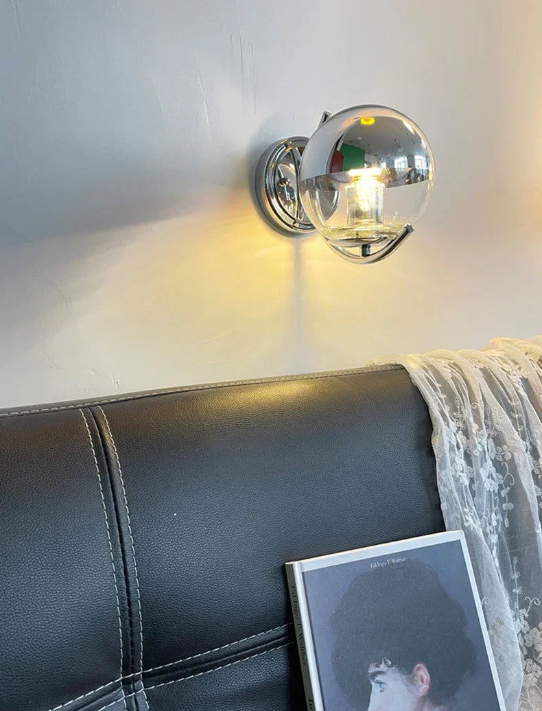 Wall-mounted chrome sconce lighting fixture on a wall above a black leather sofa with a photo on a stand.