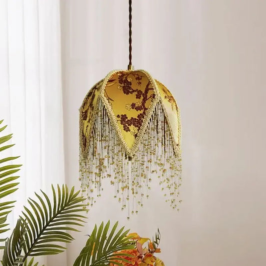 Yellow fabric pendant light with floral pattern and beaded tassels hanging indoors.