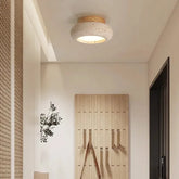 A modern hallway with a single round yellow travertine flush mount ceiling light with a wood canopy.