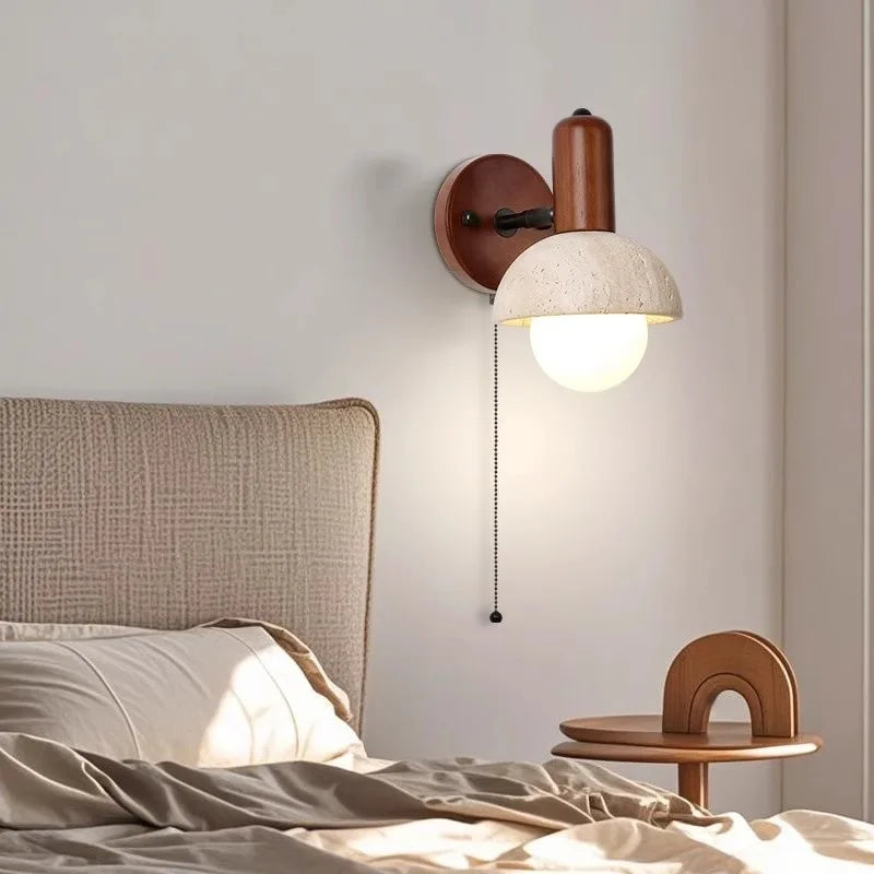 Close-up of a stone and wood wall sconce with a pull chain switch above a bed.
