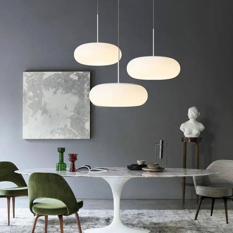 Three white oval pendant lights hanging over a dining table