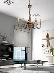A distressed wood and iron candle-style chandelier installed in a modern living room, illuminated.