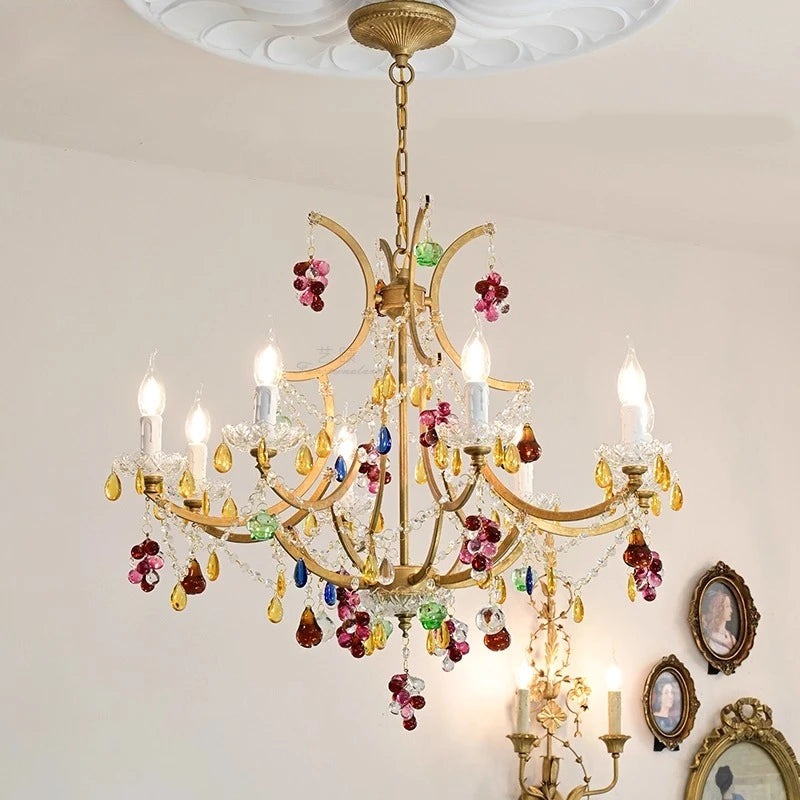 Close-up of a gold chandelier adorned with vibrant red, green, and purple crystals, with multiple light sources.