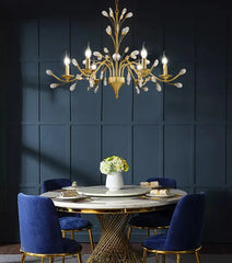 Dining room with a gold chandelier, marble table, and blue chairs against a dark paneled wall.