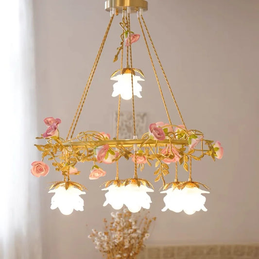 Close-up of a gold pendant light with pink rose and leaf ceramic accents, featuring a white frosted glass shade.