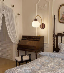 Vintage bedroom with wooden desk, bed, and wall lamp.