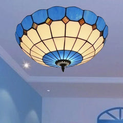 A blue stained glass ceiling light with a scalloped edge installed on a ceiling, with light emanating from it.