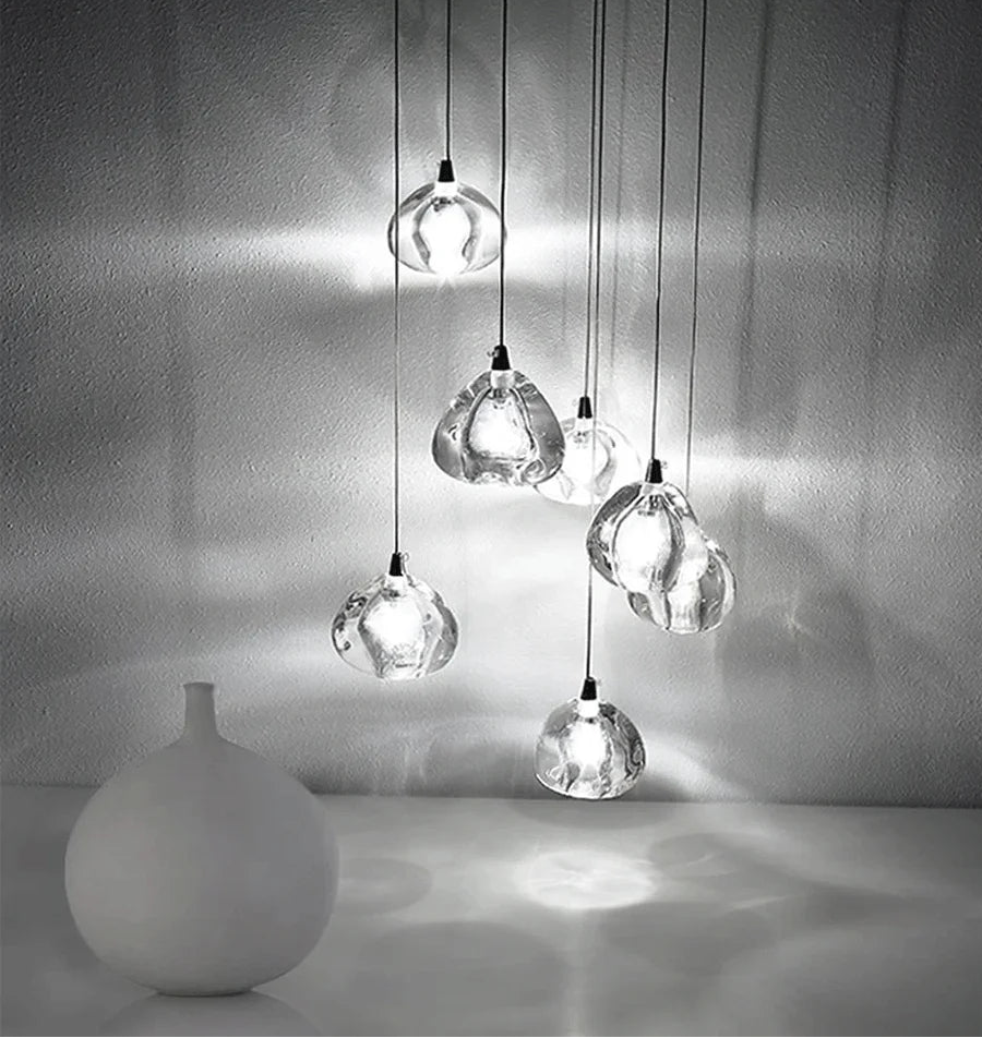 A cluster of clear crystal ball pendant lights hanging in a cascade, with a white vase in the foreground.