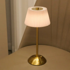 Table lamp with pleated white shade and gold base on a beige surface.
