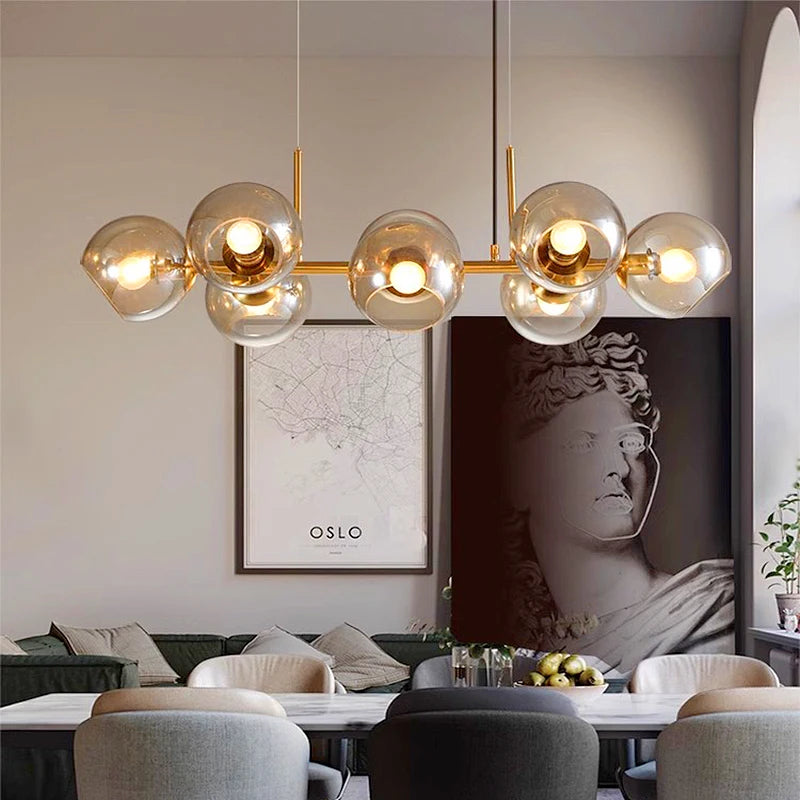 A dining room setting illuminated by a gold-toned linear chandelier with clear glass globes.