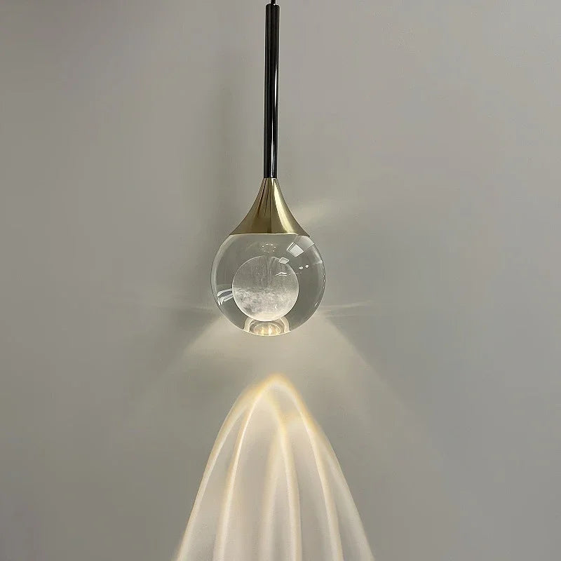 Close-up of a clear glass globe pendant light with a textured inner orb, showing the light's glow and beam pattern on a wall.
