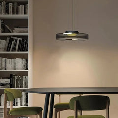 Smoke grey glass disk pendant light illuminating a dining area with a bookshelf and chairs.