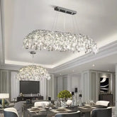 A large, multi-tiered chrome chandelier with cascading crystals over a dining room table.