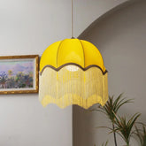 Yellow velvet dome pendant light with long cream fringe hanging from a ceiling.