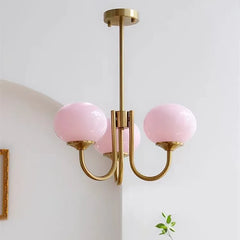 A close-up of a gold chandelier with three pink globe-shaped glass shades, mounted to a ceiling.