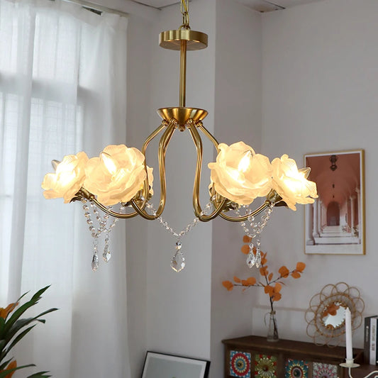 Close-up of a gold chandelier featuring detailed rose flower lampshades and sparkling crystal drops, illuminated against a soft background.