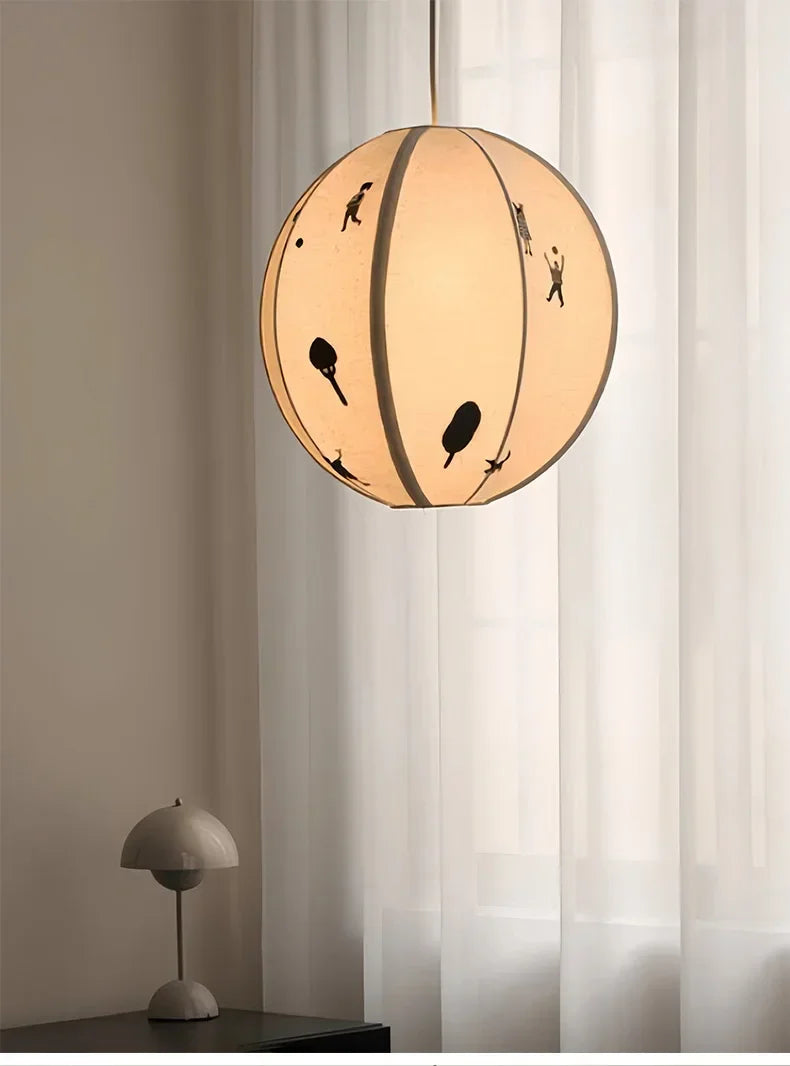 Round pendant light with black cut-out designs in a room with curtains and a small table lamp.