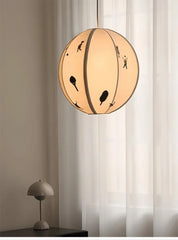 Round pendant light with black cut-out designs in a room with curtains and a small table lamp.