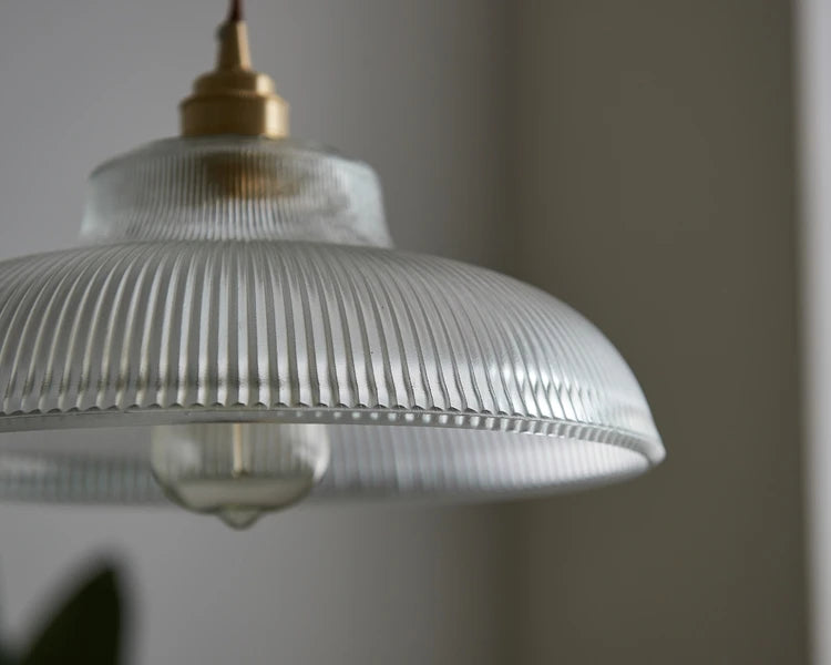Close-up of a pendant light with ribbed glass shade against a neutral background