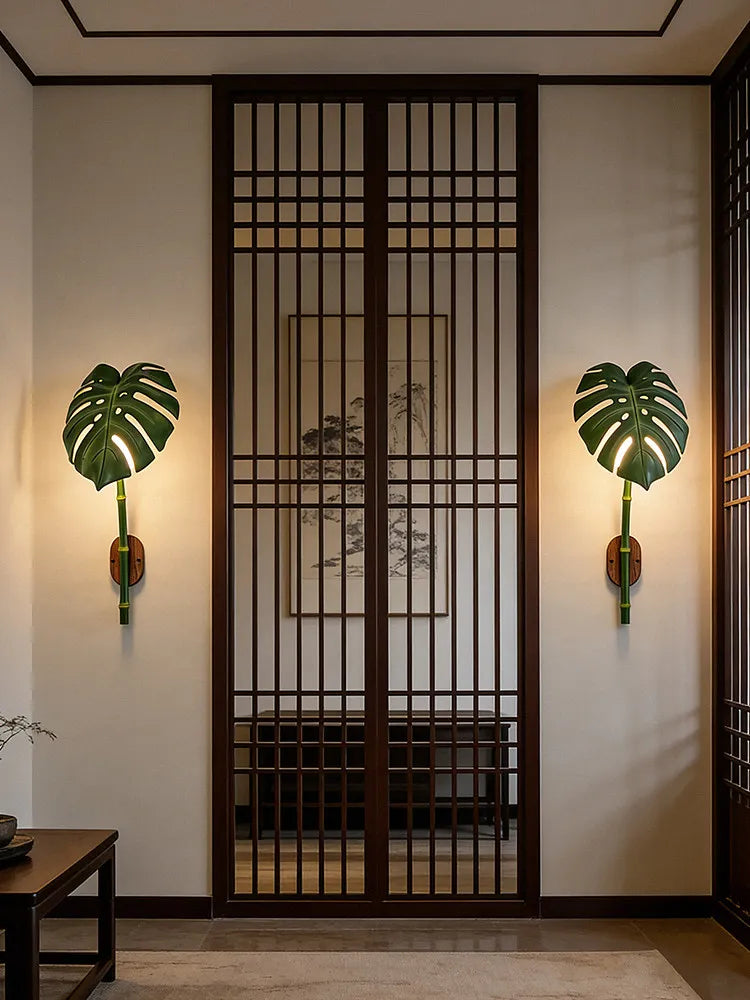 Pair of green leaf bamboo wall sconces illuminating a hallway with traditional wooden doors and artwork.