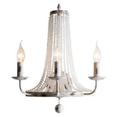 A distressed white wall sconce with a tiered design featuring cascading clear crystal beads and three candle-style light holders.