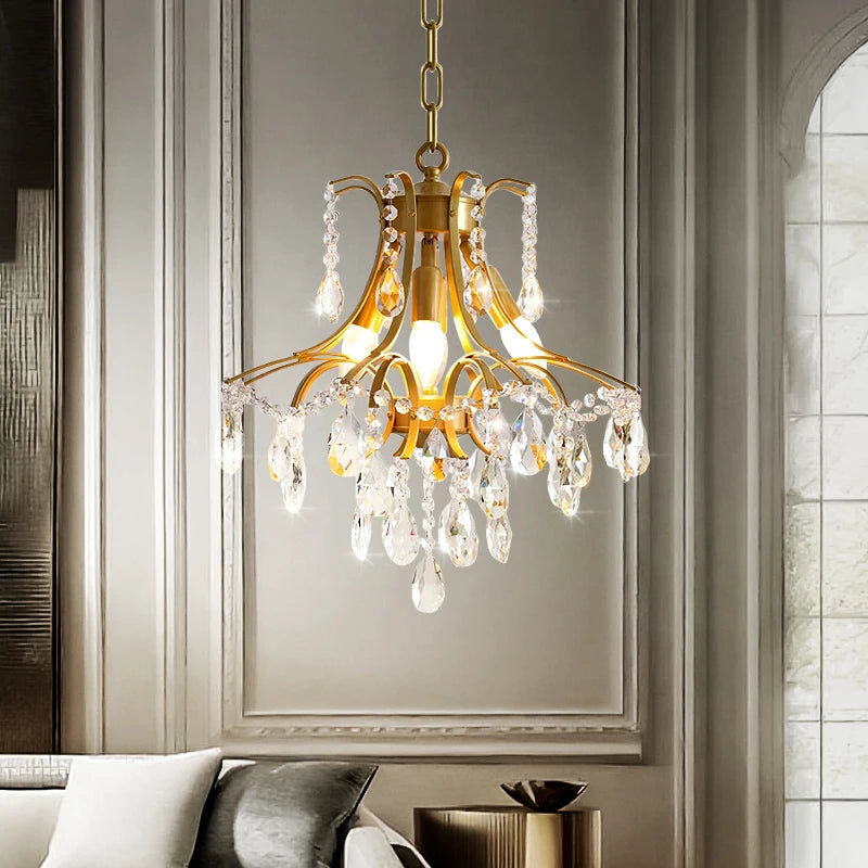 Gold chandelier with crystal accents hanging in a room with a gray wall and white ceiling.