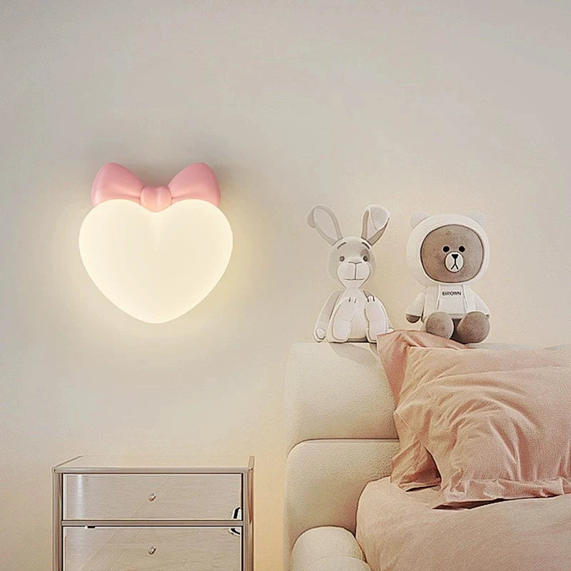 A pink bow heart-shaped wall sconce above a nightstand with stuffed animals on the bed.