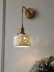 Wall-mounted lamp with decorative white shade and gold fixture on a light gray wall.