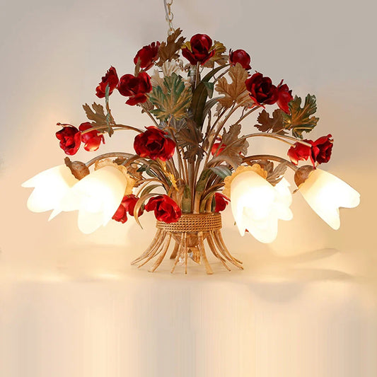 A close-up view of a gold floral pendant light with red rose buds and white tulip-shaped glass shades, against a neutral background.