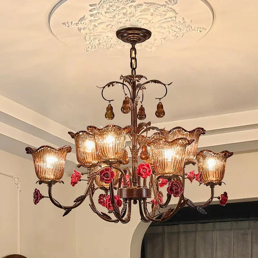 Close-up view of a bronze chandelier with red rose ceramic flowers and clear glass shades hanging from a white ceiling.