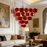 A cascading chandelier with multiple tiers of red glass discs hanging in a well-decorated living room.