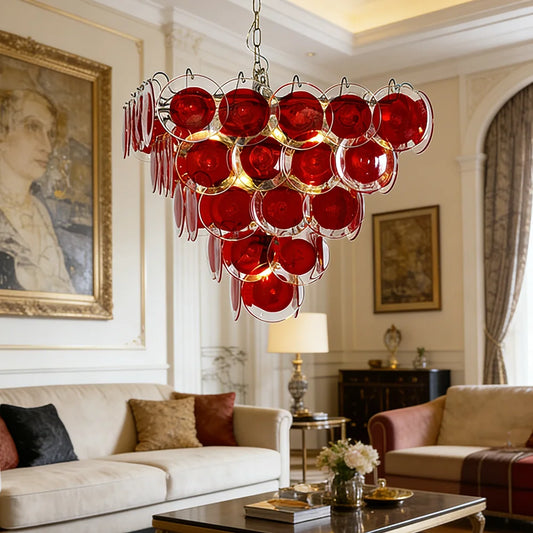 A cascading chandelier with multiple tiers of red glass discs hanging in a well-decorated living room.
