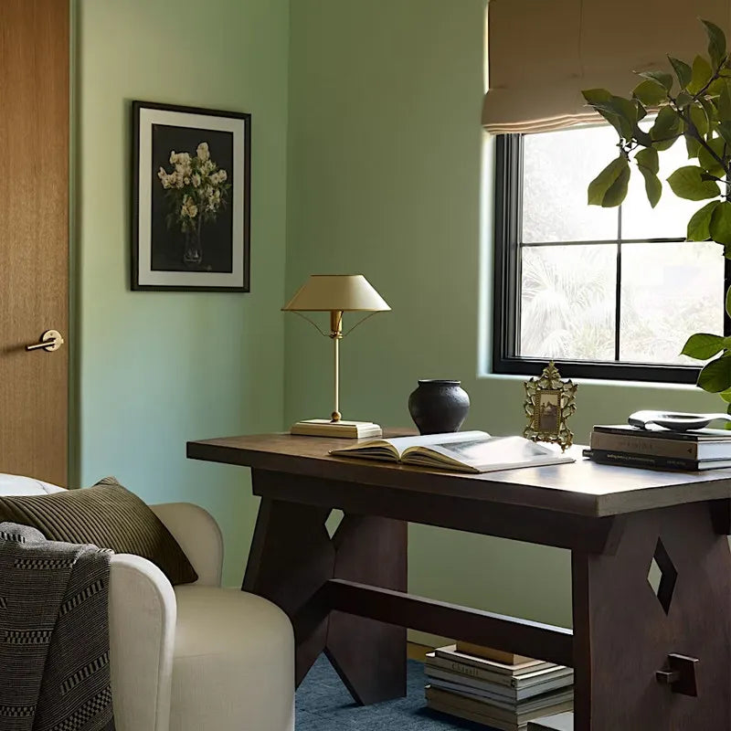 A black metal table lamp with a cone shade and polished chrome details, shown in a dimly lit room setting.