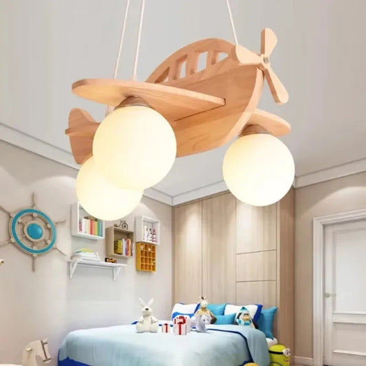 Wooden airplane pendant light with three milk white glass globes hanging in a child's bedroom with blue bedding and shelves.