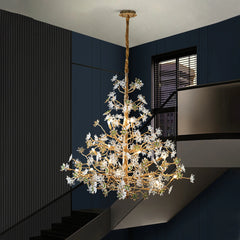 A close-up view of a gold chandelier with intricate branches adorned with clear and green crystal floral elements, suspended against a dark blue wall.