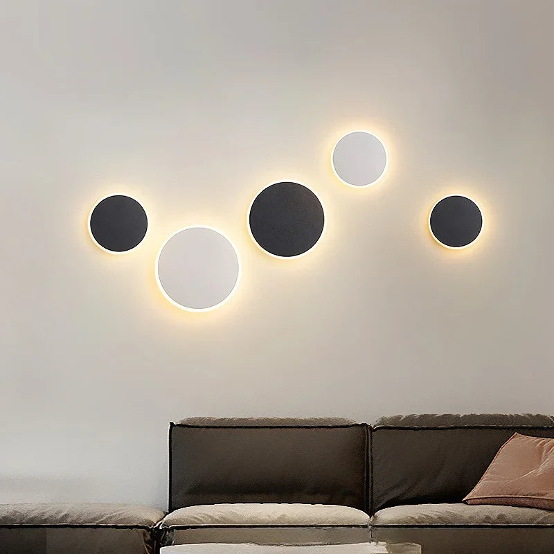 Group of circular black and white wall sconces with a warm halo effect mounted on a light-colored wall above a sofa.