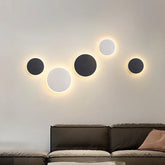 Group of circular black and white wall sconces with a warm halo effect mounted on a light-colored wall above a sofa.