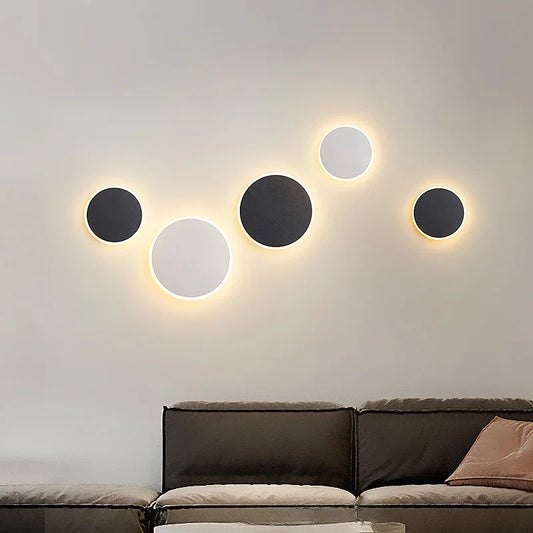 Group of circular black and white wall sconces with a warm halo effect mounted on a light-colored wall above a sofa.